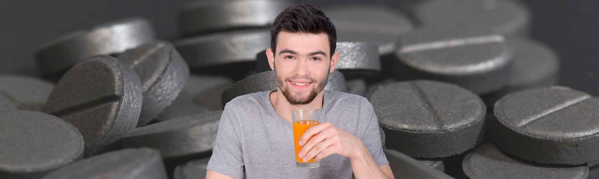 man taking activated charcoal pills with juice